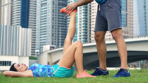 Trainer Helps Woman Stretch Leg in Park