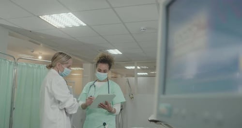 Doctor and Nurse looking at Medical Results on Digital tablet in Hospital wearing Face mask.