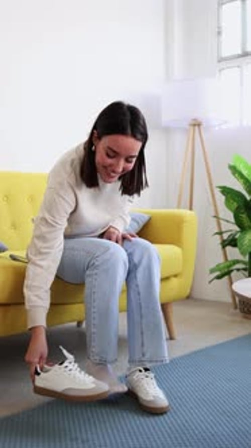 Young Woman Putting on and Taking Off Sneakers While Sitting on Yellow Armchair