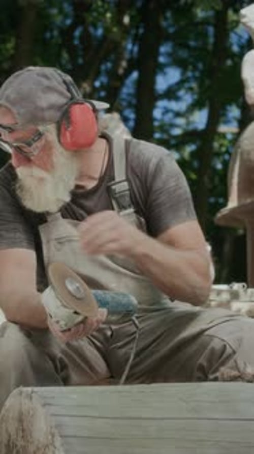 Male Sculptor Using Angle Grinder to Make Stone Sculpture Outdoors