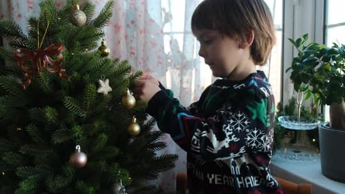 Boy Decorates Christmas Tree With Baubles at Home