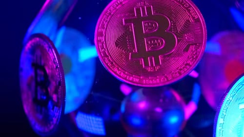 Pièces Bitcoin dans des néons violets sur fond de boule transparente à rotation lente en gros plan.