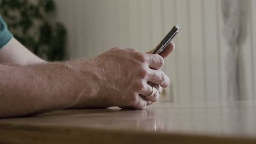 Man's Hands Using Smartphone Device on Table Indoors