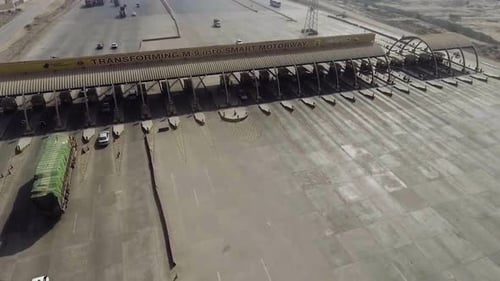 Uma vista aérea próxima de uma rodovia, praça de pedágio da cidade, veículos pesados e outros entrando e saindo