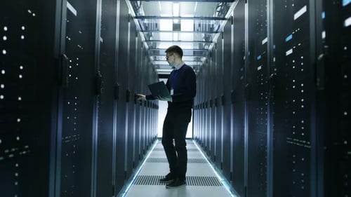 Vista frontal de un ingeniero de TI recorriendo un centro de datos lleno de servidores en rack en funcionamiento. Abre Serv