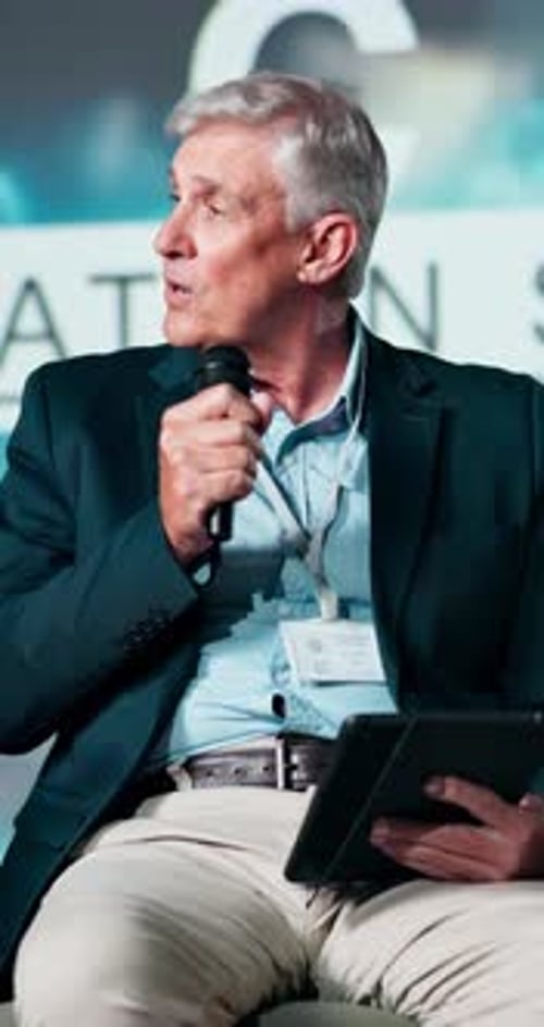 Man Speaking at Corporate Conference Holding Tablet