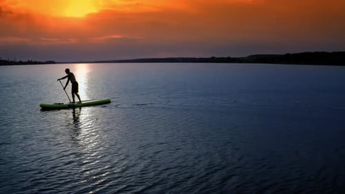 Young Man SUP Boarding. Aerial view of strong man swimming surfing boat
