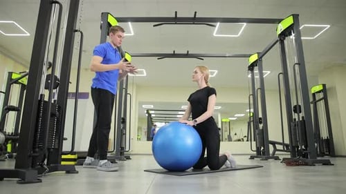 A Man Coach is Training a Woman By Using a Stability Ball in a Contemporary and Wellequipped Gym