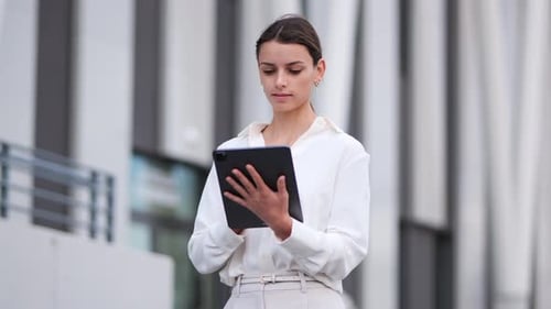 businesswoman walking past a modern building while working on her tablet