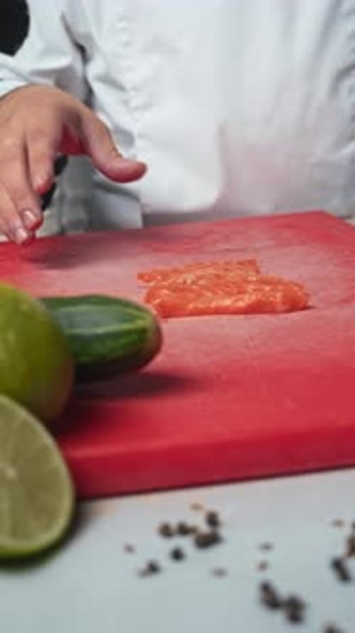 Chef Cuts Slices of Red Fish Similar to Trout Surrounded By Various Ingredients From Vegetables in
