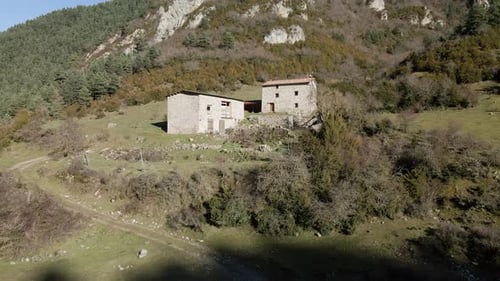 Elevating drone movement to get a good view of two abandoned farm houses in the middle of the mounta