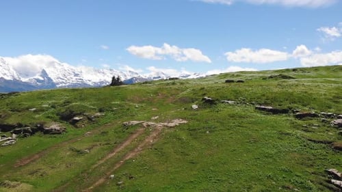 Drone view of grassy hill overlooking mountains against blue sky