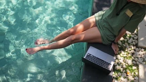 Woman Relaxing with Laptop by Tropical Swimming Pool