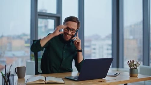 Smiling Man Works at Desk on Laptop and Phone