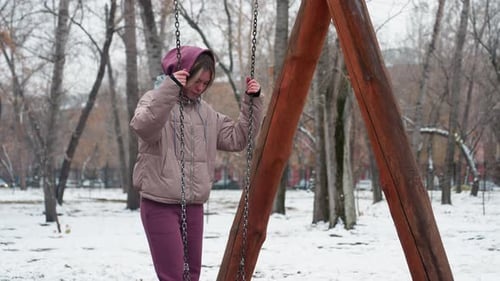 Young Woman Balancing on Iron Swing in Snowy Urban Park