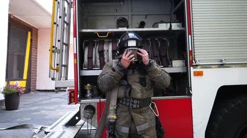 Firefighter Adjusts Mask Next to Fire Engine