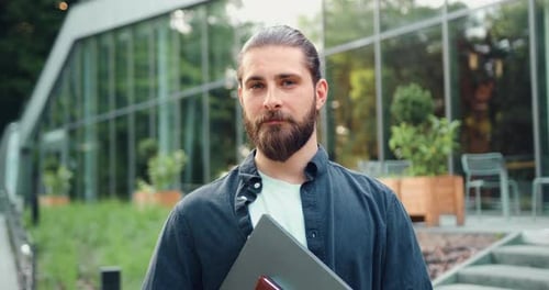 Handsome Office Worker with Laptop Standing in Cityscape and Giving a Friendly Smile to the Camera