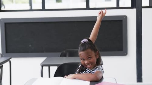 In a school classroom, a young African American girl raises her hand
