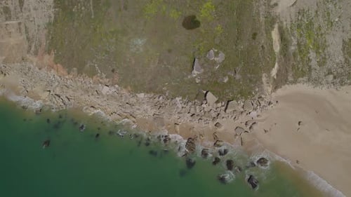 Aerial top-down shot of the calm ocean waves crashing on the rocky coastal shore in Nazare, Portugal
