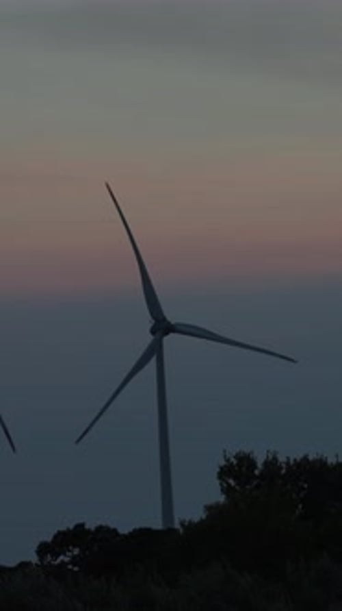 Wind Turbines Silhouetted Against Colorful Sky At Sunset