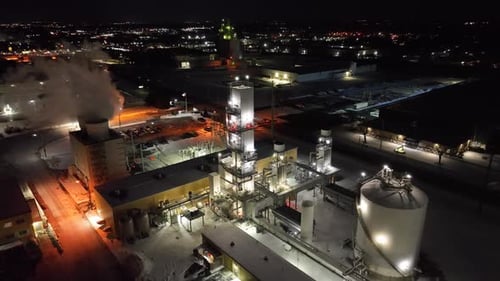 Vapor tóxico de una planta química que se eleva hacia el cielo nocturno. Ondeando la bandera estadounidense e iluminando la ciudad al fondo