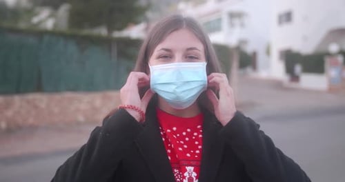 Young woman taking off her surgical mask in the street. Coronavirus (Covid-19) pandemic.