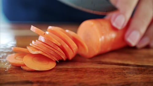 Close up of a woman cutting up a carrot on a wooden cutting board