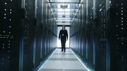 Vista frontal de un ingeniero de TI recorriendo el centro de datos con servidores en rack en funcionamiento.