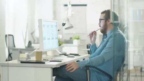 Bearded Man Thoughtfully Working at Computer in Office