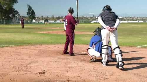Playing baseball, batter in maroon uniform preparing to hit pitch on field