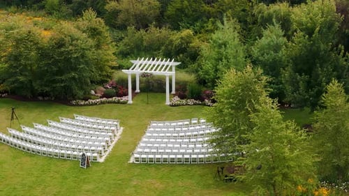 The Aerial Drone View of the Outdoor Wedding Setup with Rows of White Chairs Facing a Wooden Arch