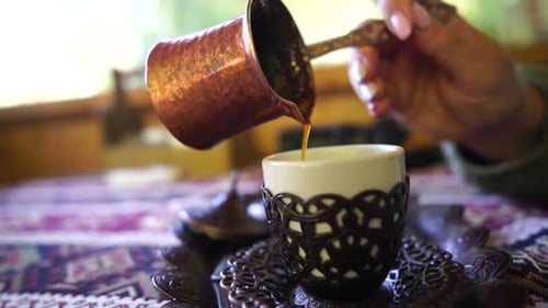 Woman Pours Coffee into Decorative Cup from Pot