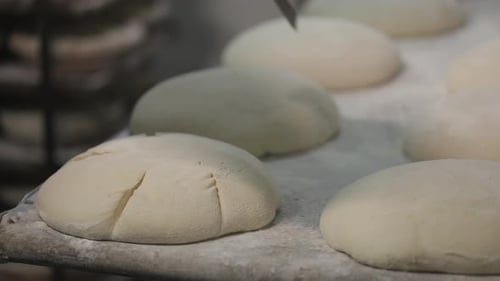 The process of making bread in a bakery. After proofing, the top of the bread is cut with knife.