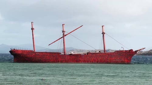 Seitenansicht eines rostigen alten Schiffswracks, das im blauen Wasser liegt.