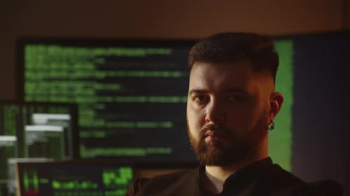 Bearded Programmer Posing with Computer Screens on the Background Hacker is Breaking the Code