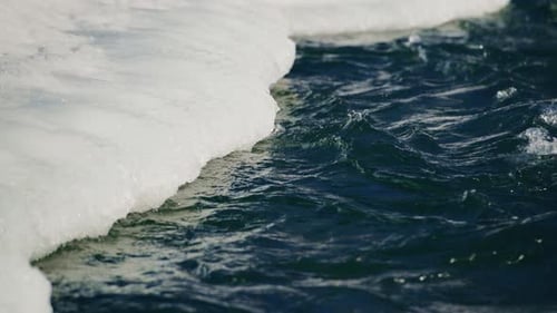 Gentle Waves Gracefully Lapping Rhythmically Against the Ice Edge in a Tranquil Winter Landscape