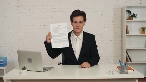 Medium Video of a Young Man Sitting at the Table in the Office Holding a Contract in His Hands