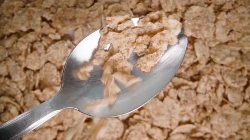 Cornflakes zum Frühstück fallen von oben auf einen Löffel, darunter ein Flockenhintergrund.
Zeitlupe