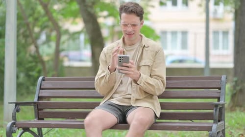 Young Man Using Smartphone on Park Bench