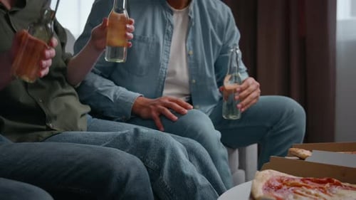Gros plan : quatre amis méconnaissables qui tintent des bouteilles à la maison, en partie en train de boire de la bière et de l'alcool