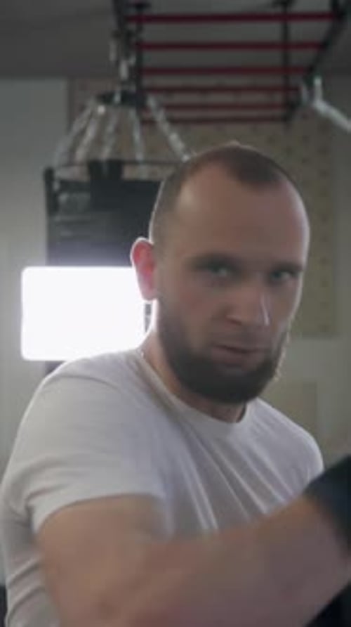 Motivated man in sportswear practicing punches during training. Boxer punching air in gym close-up.