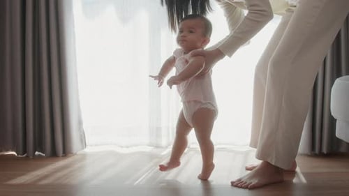 A baby girl learning first steps walk with mother, family, child, childhood and parenthood concept