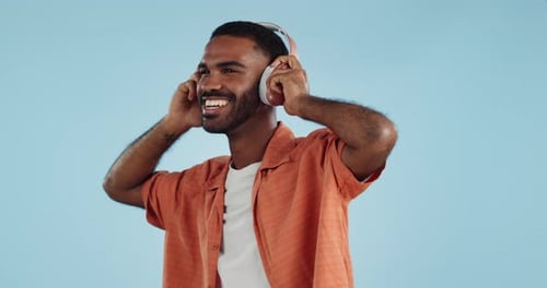 Black man, headphones and dancing to music with happiness and energy in studio on blue background