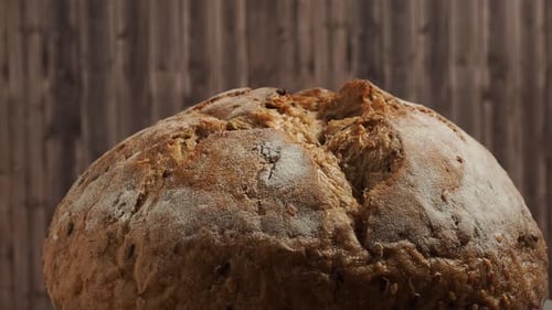 Rotation of dark bread on a wooden background. Round bread with grains. Close-up.
