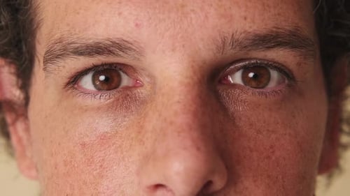 Detailed close-up shot of man's eye looking at the camera studio on beige background