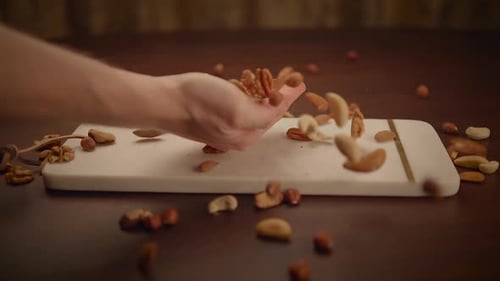 Hand Holding Nuts Cascading to Cutting Board