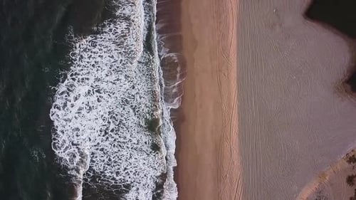 Vertical air view of waves hitting the beach with nobody