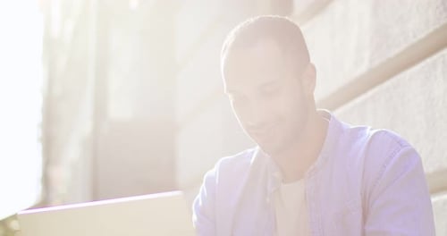 Close Up of Happy Handsome Young Man Sitting at Table of Cafe in City Center with Laptop and Typing