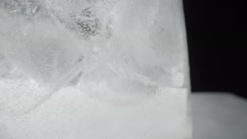 Ice cubes in a soda glass and bubbles rise up, macro on a black background.