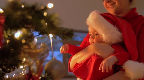 Mother holds baby near Christmas tree indoors